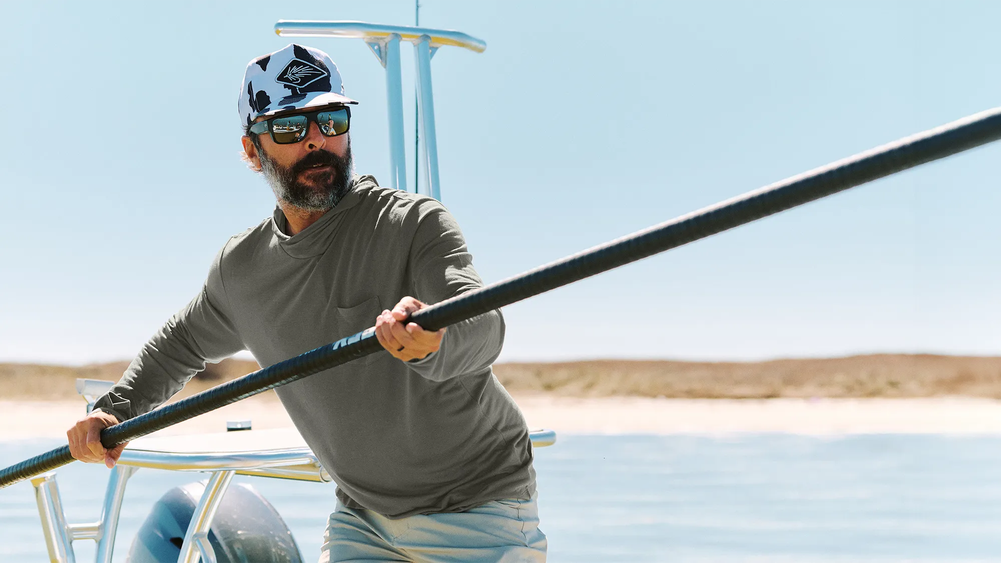 Man on a boat holding a long pole with a clear sky and water background