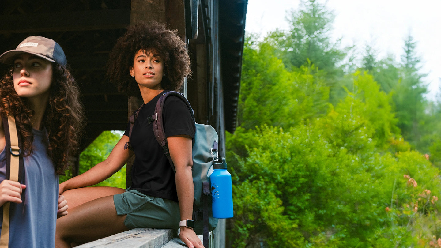 Two women with backpacks sitting on a vehicle in a forest setting