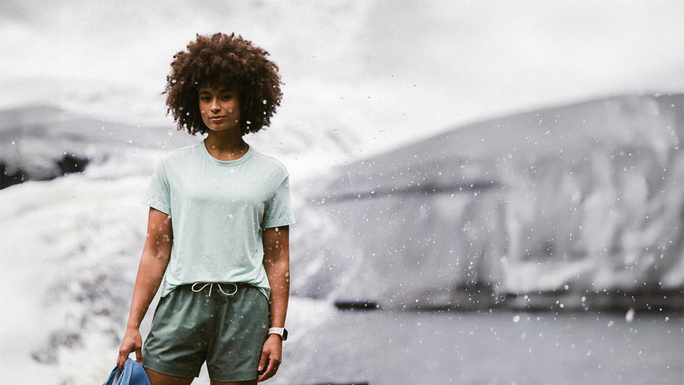 Person standing in a snowy landscape wearing a light green t-shirt and shorts.